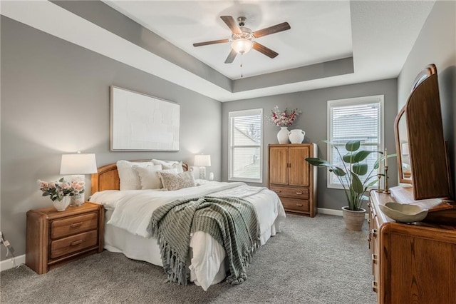 bedroom featuring a tray ceiling, light carpet, baseboards, and multiple windows