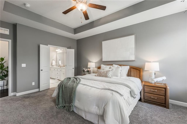 bedroom featuring carpet floors, visible vents, baseboards, a tray ceiling, and ensuite bath