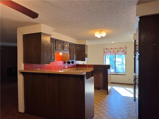 kitchen with a breakfast bar area, dark brown cabinetry, a textured ceiling, decorative backsplash, and kitchen peninsula