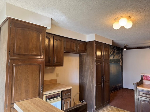 kitchen featuring white oven, a textured ceiling, and dark brown cabinetry