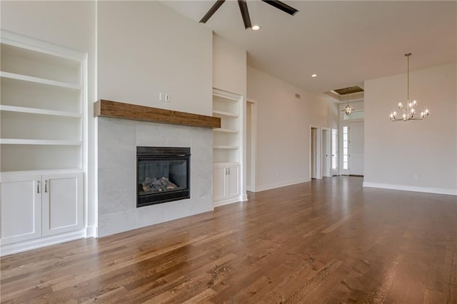 unfurnished living room featuring built in shelves, ceiling fan, wood-type flooring, and a tiled fireplace