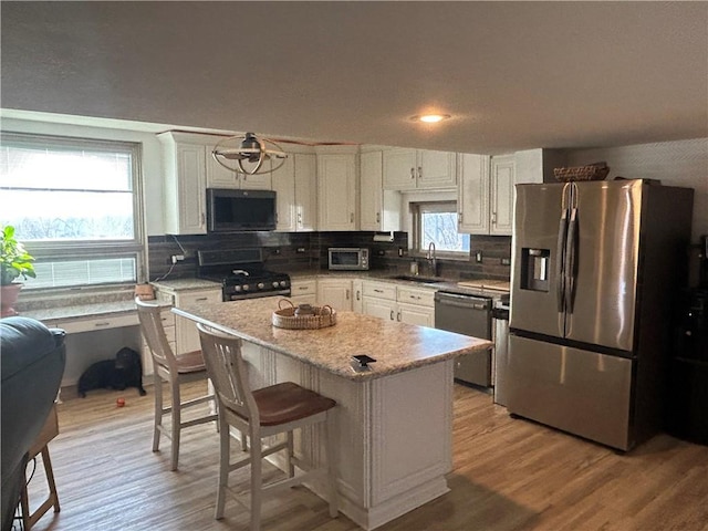 kitchen featuring backsplash, appliances with stainless steel finishes, a sink, light wood finished floors, and white cabinetry