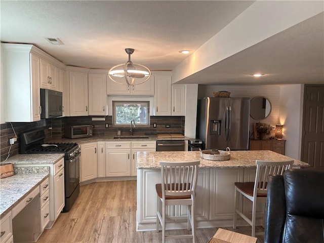 kitchen with visible vents, black gas stove, stainless steel fridge, white cabinets, and a sink
