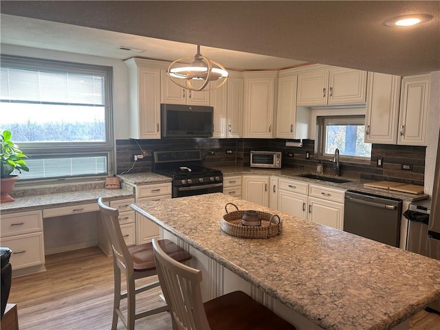 kitchen with black microwave, stainless steel range with gas stovetop, a sink, dishwashing machine, and light wood-style floors