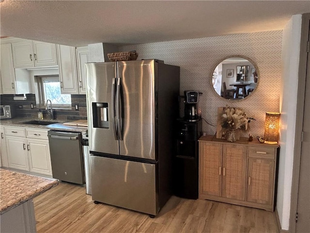 kitchen featuring a sink, appliances with stainless steel finishes, light wood-style flooring, and white cabinetry