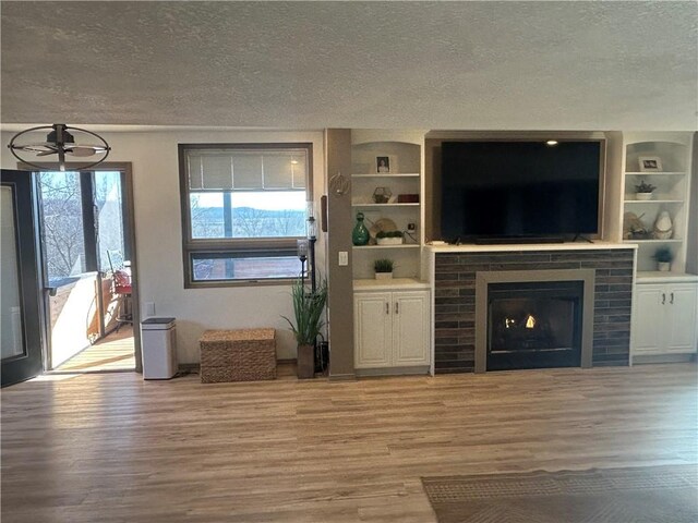 unfurnished living room featuring light wood-style flooring, a textured ceiling, and built in features