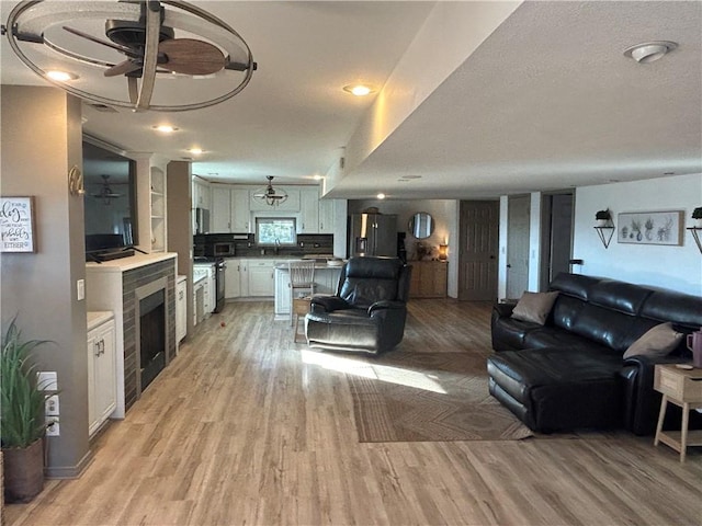 living room with light wood finished floors, ceiling fan, and a fireplace