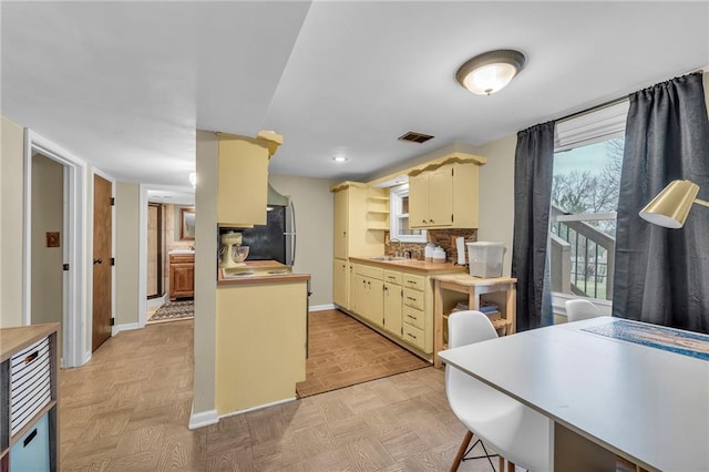 kitchen with a breakfast bar area, tasteful backsplash, stainless steel refrigerator, cream cabinets, and light parquet floors