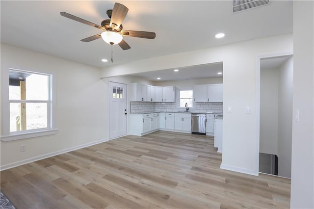 kitchen with tasteful backsplash, visible vents, stainless steel dishwasher, white cabinetry, and a sink