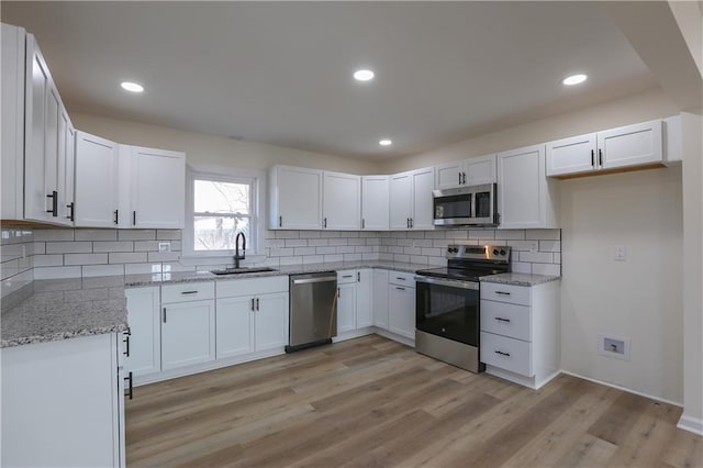 kitchen featuring light stone counters, stainless steel appliances, a sink, white cabinets, and light wood finished floors