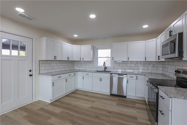 kitchen featuring light stone counters, light wood-style flooring, a sink, visible vents, and appliances with stainless steel finishes