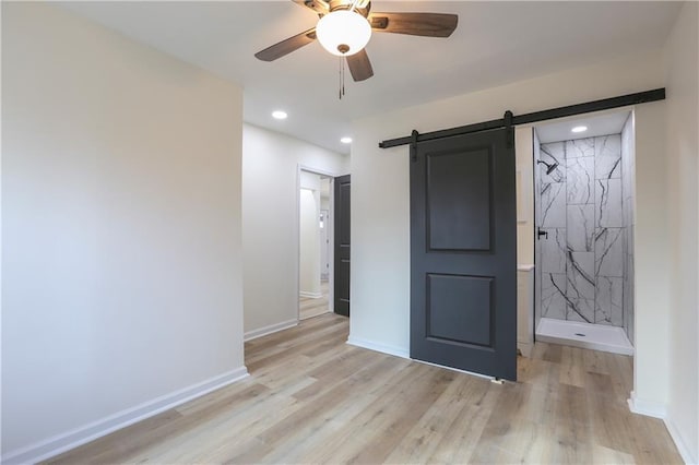 unfurnished bedroom featuring a barn door, light wood-type flooring, and baseboards