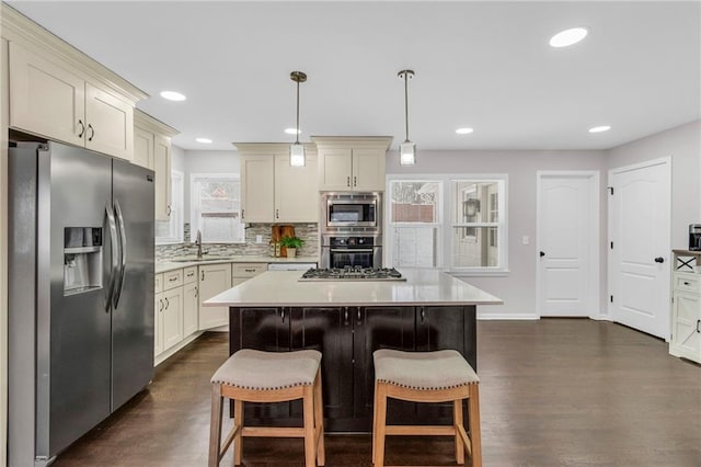 kitchen with dark wood finished floors, a breakfast bar, stainless steel appliances, light countertops, and backsplash