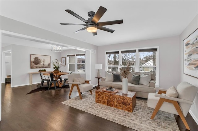 living area with baseboards, dark wood-style flooring, and ceiling fan with notable chandelier