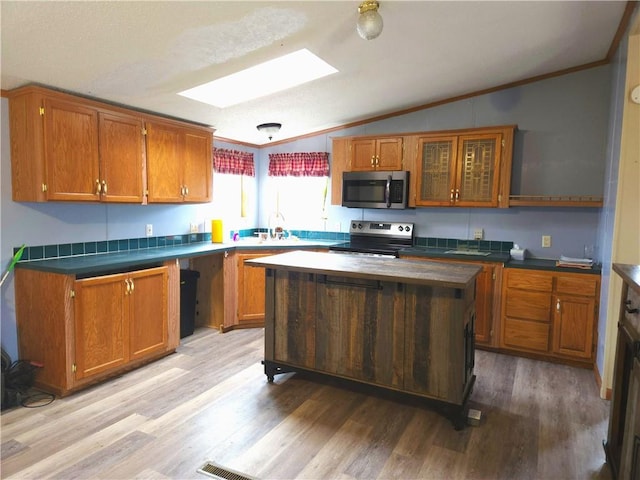 kitchen with lofted ceiling with skylight, a kitchen island, ornamental molding, stainless steel appliances, and light hardwood / wood-style flooring