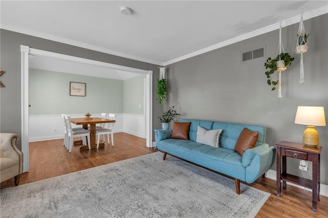 living area with visible vents, crown molding, baseboards, and wood finished floors