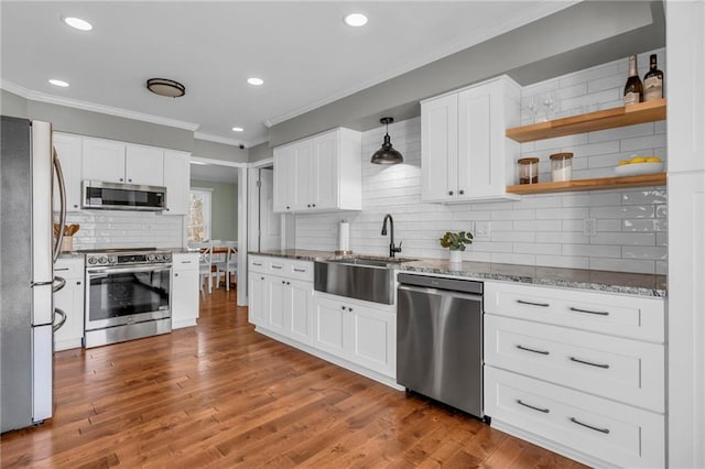 kitchen featuring ornamental molding, a sink, wood finished floors, stainless steel appliances, and stone counters