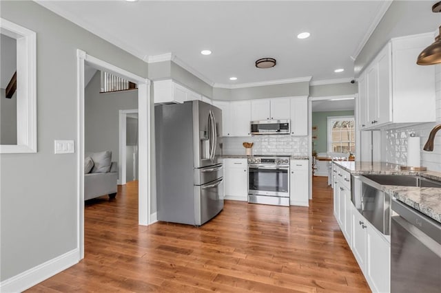 kitchen with light stone counters, light wood-style flooring, appliances with stainless steel finishes, white cabinetry, and crown molding