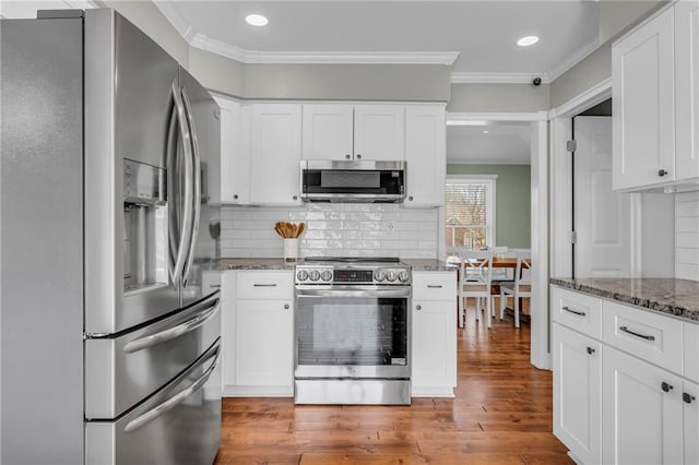 kitchen with dark stone counters, ornamental molding, wood finished floors, and stainless steel appliances