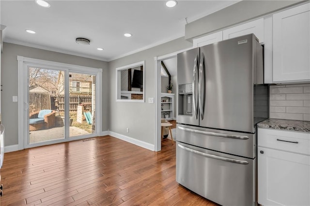 kitchen featuring backsplash, crown molding, white cabinets, hardwood / wood-style flooring, and stainless steel fridge