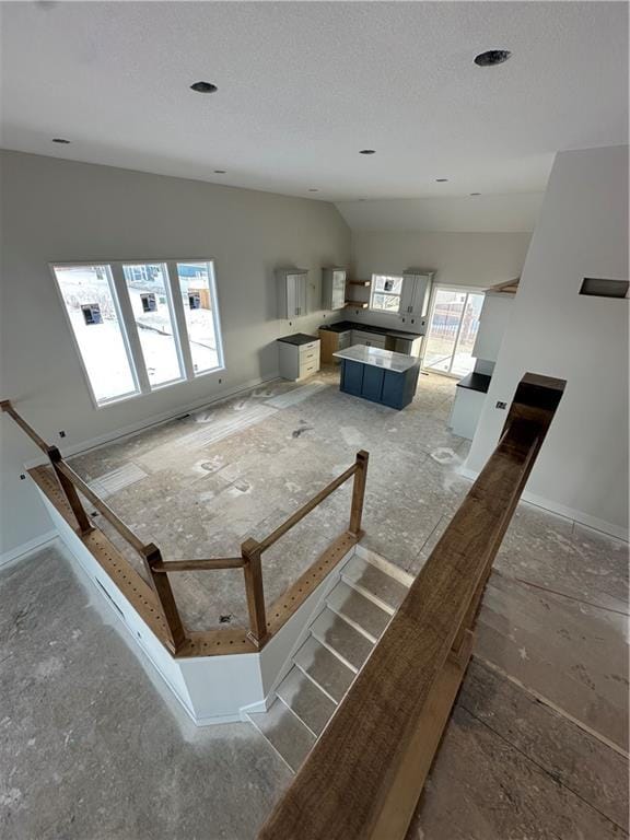 unfurnished living room with baseboards, vaulted ceiling, and a textured ceiling