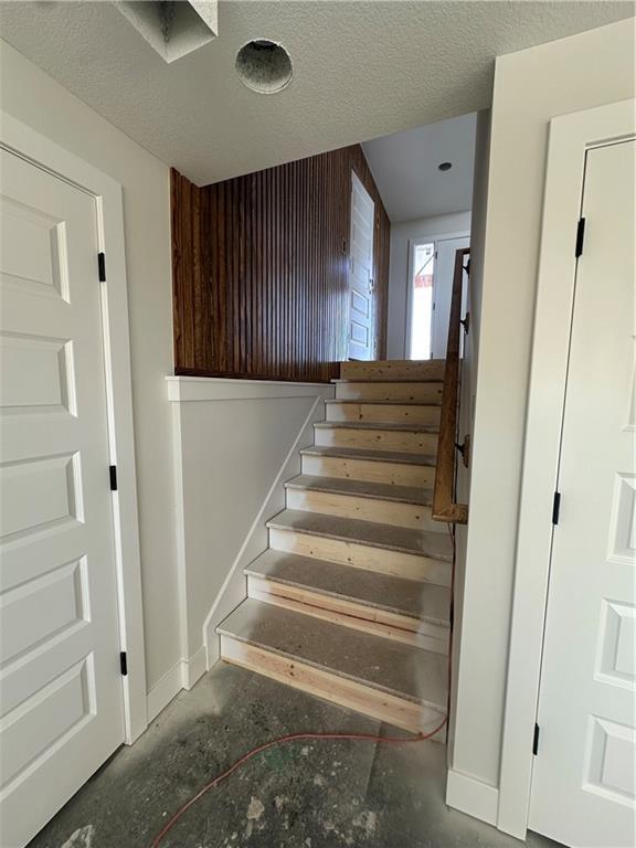 stairway featuring concrete floors, baseboards, and a textured ceiling