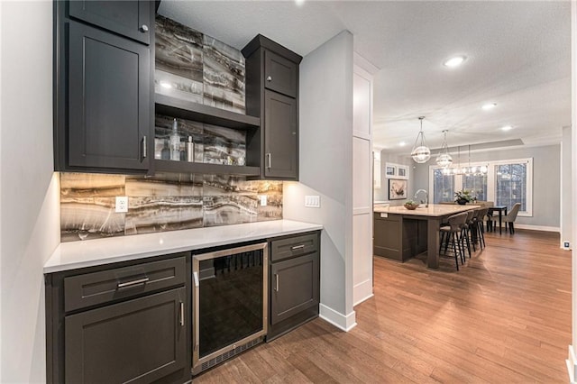 bar with wine cooler, tasteful backsplash, hanging light fixtures, and hardwood / wood-style flooring