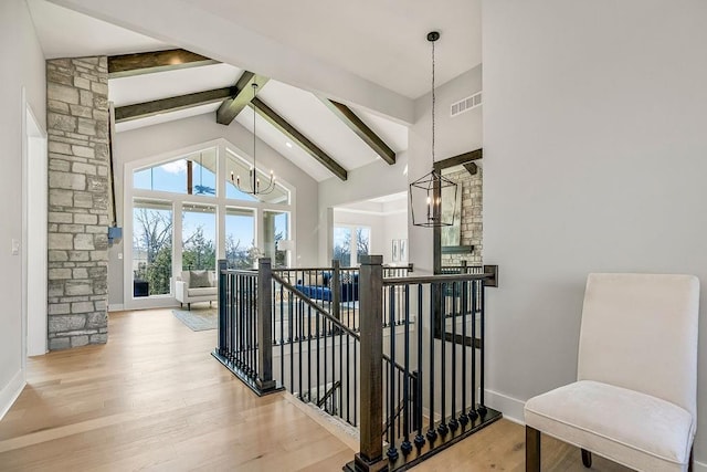 stairway featuring a healthy amount of sunlight, wood-type flooring, beamed ceiling, and a chandelier