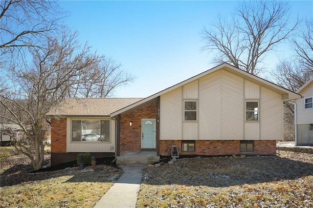 split level home featuring roof with shingles and brick siding