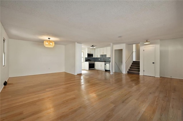 unfurnished living room featuring light wood finished floors, stairs, a sink, and a textured ceiling