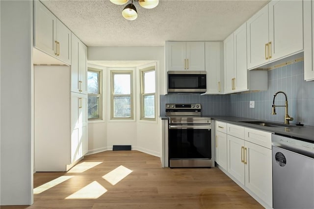 kitchen with stainless steel appliances, tasteful backsplash, light wood-style flooring, white cabinetry, and a sink