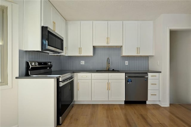 kitchen featuring stainless steel appliances, dark countertops, light wood-style floors, white cabinets, and a sink