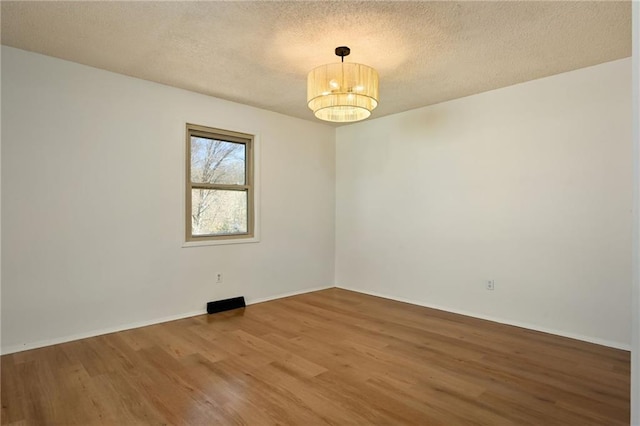 spare room with an inviting chandelier, a textured ceiling, baseboards, and wood finished floors