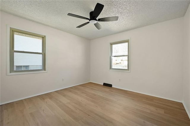 empty room with visible vents, a ceiling fan, a textured ceiling, light wood-type flooring, and baseboards