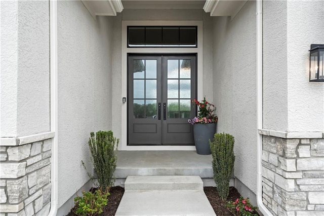 entrance to property with french doors, stone siding, and stucco siding