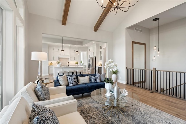 living room featuring lofted ceiling with beams, a chandelier, and light hardwood / wood-style floors