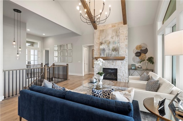 living room with beamed ceiling, a stone fireplace, light hardwood / wood-style floors, and a notable chandelier