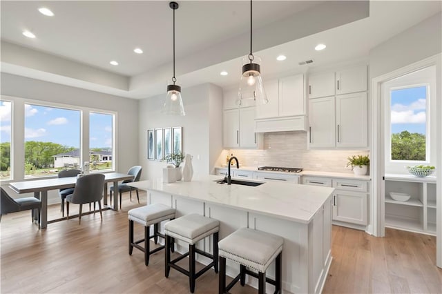 kitchen with pendant lighting, sink, a center island with sink, and white cabinets