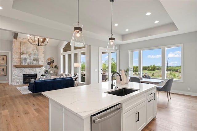 kitchen with sink, a tray ceiling, white cabinets, a center island with sink, and stainless steel dishwasher