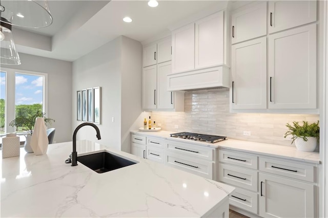 kitchen with sink, backsplash, white cabinets, stainless steel gas cooktop, and light stone counters