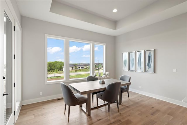 dining area featuring a raised ceiling and light wood-type flooring