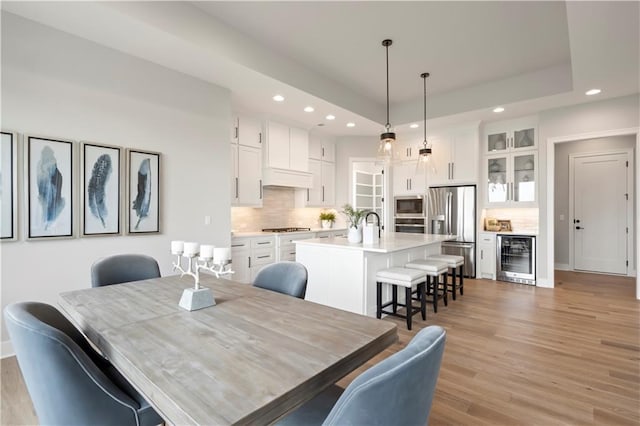 dining room featuring beverage cooler, a raised ceiling, and light hardwood / wood-style floors