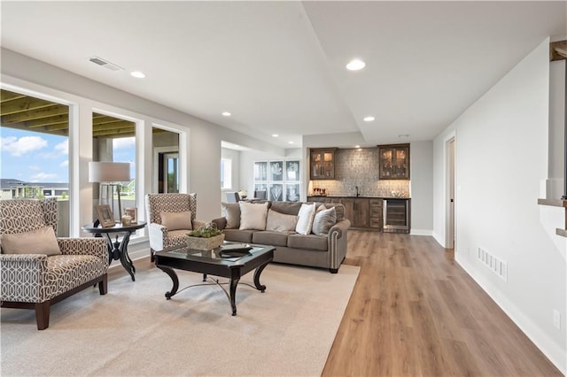 living room featuring wine cooler, light hardwood / wood-style floors, and bar