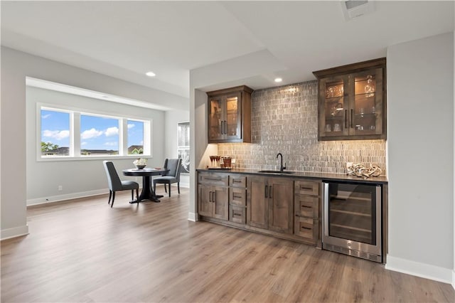 bar with sink, light hardwood / wood-style flooring, backsplash, wine cooler, and dark brown cabinetry