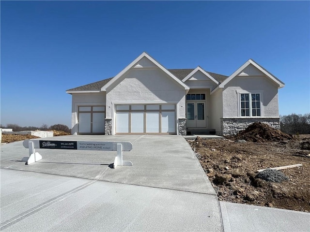 view of front of home with concrete driveway, stucco siding, french doors, a garage, and stone siding