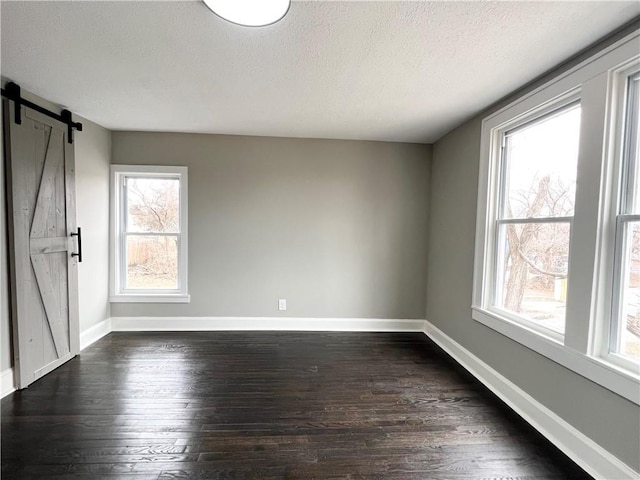 unfurnished room featuring dark hardwood / wood-style flooring, a barn door, and a textured ceiling