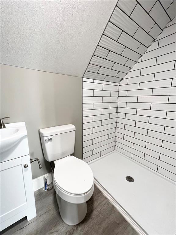 bathroom with lofted ceiling, wood-type flooring, vanity, and a tile shower