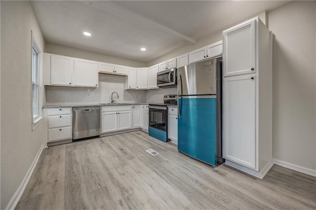 kitchen with sink, light wood-type flooring, appliances with stainless steel finishes, decorative backsplash, and white cabinets