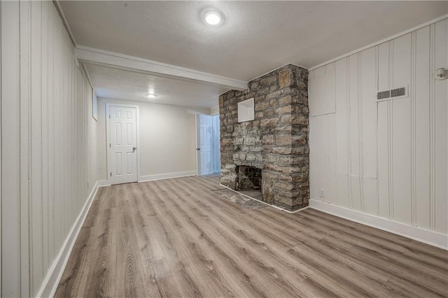 unfurnished living room with beamed ceiling, a stone fireplace, light hardwood / wood-style floors, and a textured ceiling