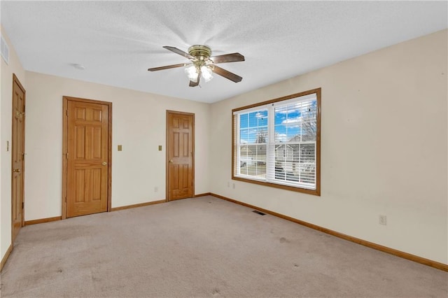 empty room with ceiling fan, light colored carpet, and a textured ceiling